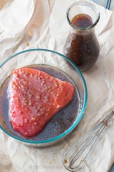 a piece of meat in a glass bowl next to a jar of ketchup