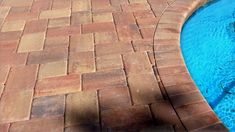 a brick patio next to a pool with blue water in the middle and an orange fire hydrant on the side