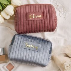 two personalized cosmetic bags sitting next to each other on a white bed with flowers