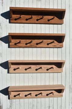 three wooden shelfs with hooks on them against a white wall in the daytime sun