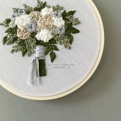 a close up of a embroidery on a wall hanging with flowers and leaves in it