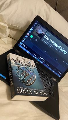 an open laptop computer sitting on top of a bed next to a book titled the naked king