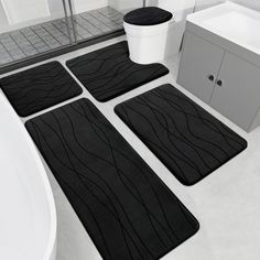 four black bath mats sitting on top of a bathroom floor next to a white tub