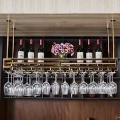 wine glasses and bottles are lined up on a shelf above a bar with wooden shelves