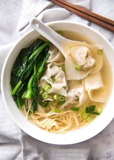 a white bowl filled with noodles, broccoli and dumplings on top of a table