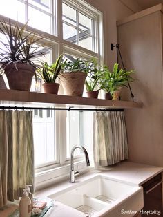 some plants are sitting on the window sill above a sink in a small kitchen