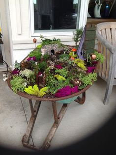 an old wheelbarrow filled with plants sitting on the front porch next to a chair