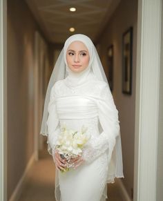 a woman in a white wedding dress holding a bouquet of flowers and wearing a veil