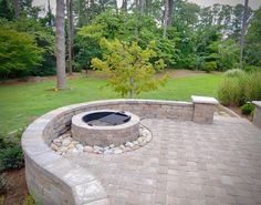 an outdoor fire pit surrounded by brick walls and landscaping area with trees in the background