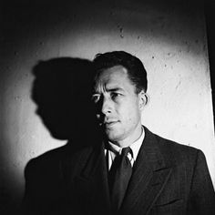 a black and white photo of a man in a suit with his shadow on the wall