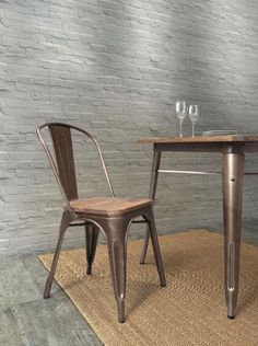 two chairs and a table in front of a brick wall with wine glasses on it