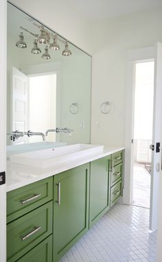 a bathroom with green cabinetry and white tile flooring, along with a large mirror on the wall