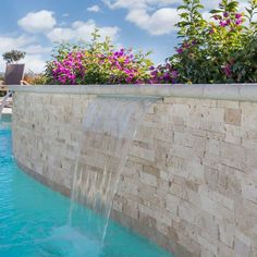 an outdoor swimming pool with a waterfall in the middle and flowers growing on the side