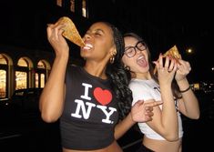 two young women eating pizza outside at night