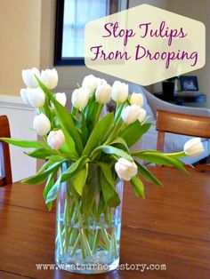 a vase filled with white tulips sitting on top of a wooden dining room table