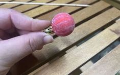 a person is holding a small pink object in their left hand, on top of a wooden bench