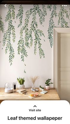 a wooden table with plates and cups on it in front of a wall painted with green leaves