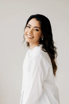 a woman with long dark hair wearing a white shirt and jeans, smiling at the camera