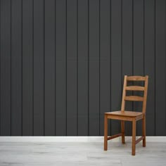 a wooden chair sitting in front of a black wall with vertical stripes on it's side