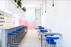 blue stools are lined up along the bar in this modern restaurant with white walls and flooring