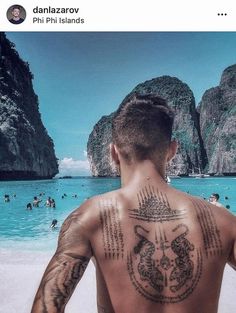 a man with tattoos on his back standing in front of the ocean and people swimming