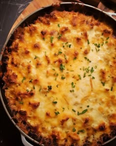 a cheesy casserole is shown in a pan on a wooden table