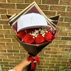 a person holding a bouquet of roses with a hat on it's head and red ribbon around its neck