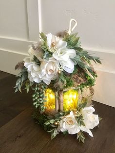 a decorative lantern with flowers and greenery on the top sits on a wooden floor