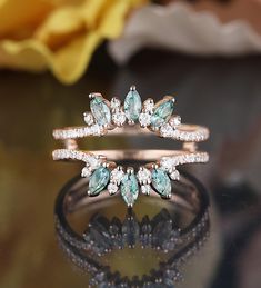 two wedding rings with green and white stones on them sitting on a table next to a yellow flower