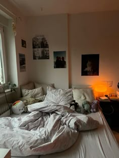 an unmade bed in a bedroom with pictures on the wall above it and stuffed animals