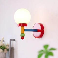 a red and yellow wall light hanging from the side of a white wall next to a potted plant