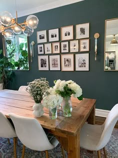 a dining room table with vases and flowers on it in front of framed pictures