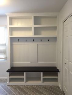 an empty room with white shelves and black bench in the center, next to a door