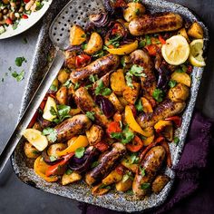 a platter filled with sausages and vegetables next to a bowl of lemon wedges