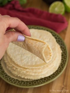 a hand holding a tortilla over a stack of corn tortillas on a green plate