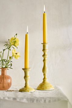 two yellow candles sitting on top of a table next to vases filled with flowers