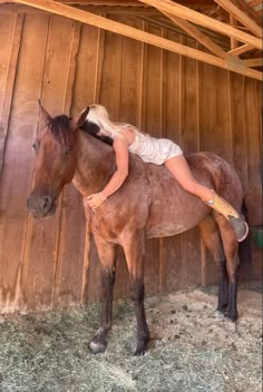 a woman is riding on the back of a brown horse in a barn with hay