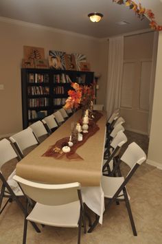 a long table with white chairs and a brown table cloth on it in front of a bookshelf