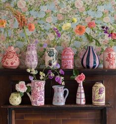 colorful vases and flowers sit on a mantle in front of a floral wallpaper