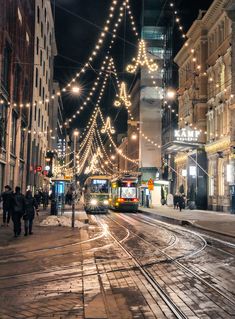 a city street filled with lots of traffic next to tall buildings covered in christmas lights