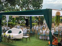 a group of people sitting around tables and chairs under a tent with green drapes