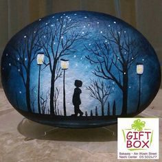 a painted rock with a boy holding a lantern in the night sky and trees on it