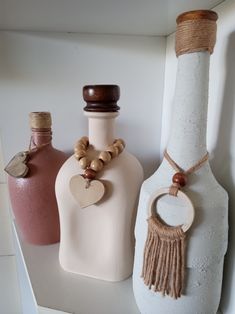 three bottles are sitting on a shelf with wooden beads and necklaces hanging from them