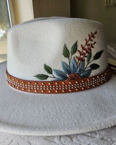 a white hat with flowers on it sitting on top of a table next to a window