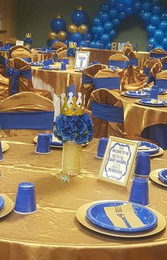 a table set up with blue and gold plates, napkins, and centerpieces