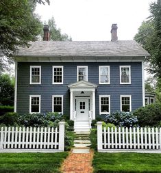 a blue house with white picket fence in front of it and trees around the yard