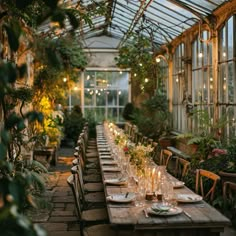 a long table set up for dinner in a greenhouse with candles and greenery on the tables