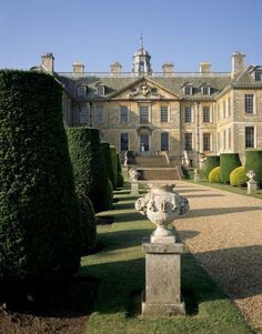 a large building with many trees and bushes in front of it, surrounded by hedges