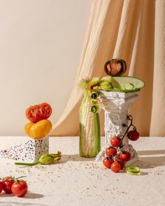 tomatoes, corn and cucumbers are arranged on a white tablecloth next to an arrangement of vegetables