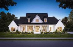 a white house with black roof and windows on the front lawn at night in an upscale neighborhood